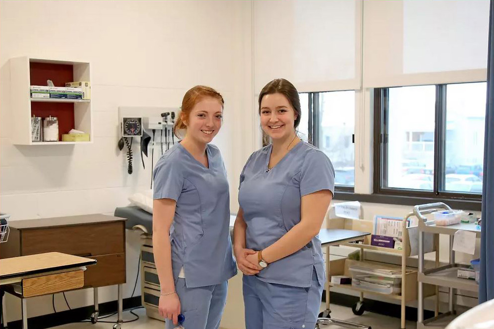 Deux étudiantes de Soins infirmiers en vêtement de travail devant un lit d'hôpital dans la clinique