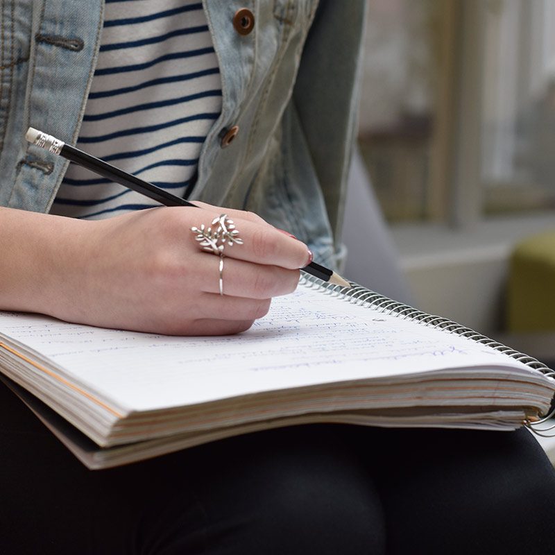 Gros plan sur une main d'étudiante qui écrit dans un cahier ligné avec un crayon de bois
