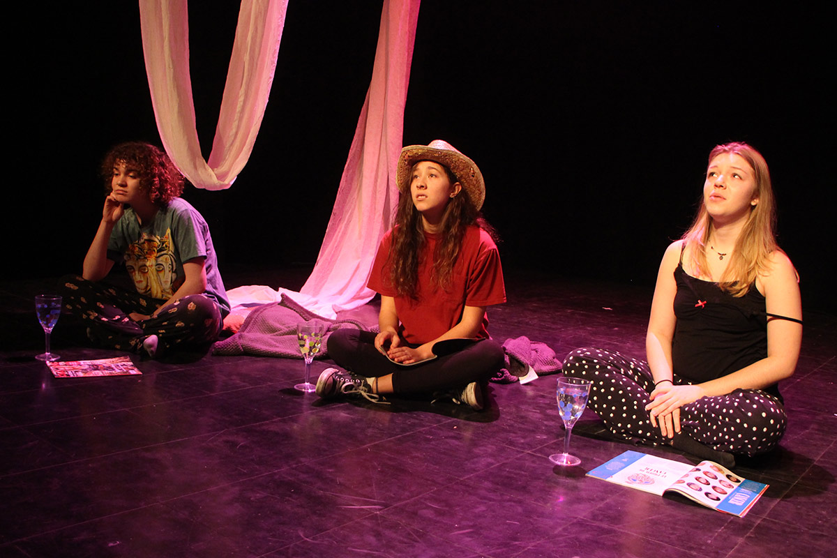 Assises par terre sur la scène, trois jeunes femmes aux visages tristes
