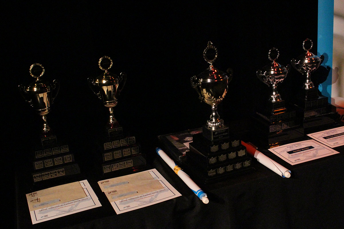 Table avec une nappe noire où sont posés cinq trophées, des certificats, des enveloppes et des bannières