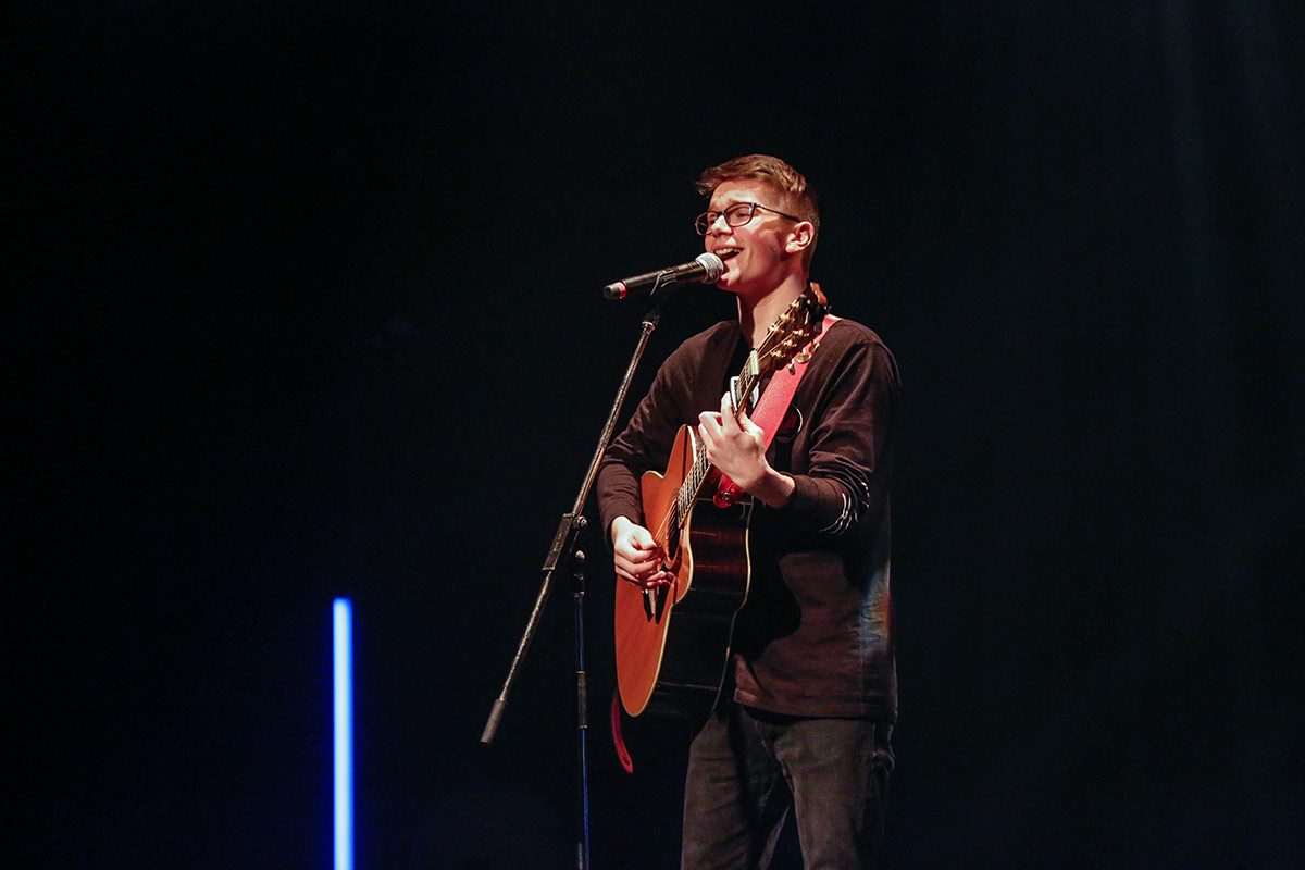 Sur la scène, Arnaud Quintal-Émard chante en s'accompagnant à la guitare