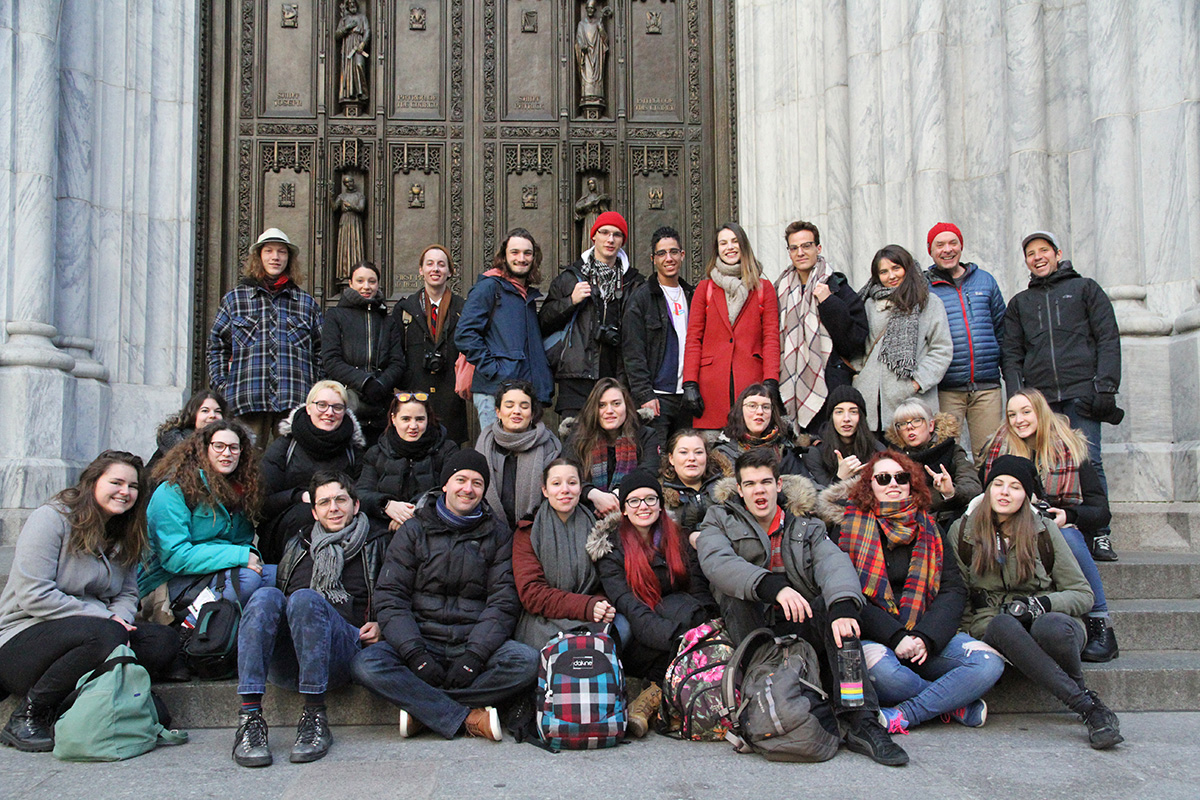 Photo d'un groupe d'étudiants et étudiantes assis à l'entrée d'une église de New York en arrière plan.