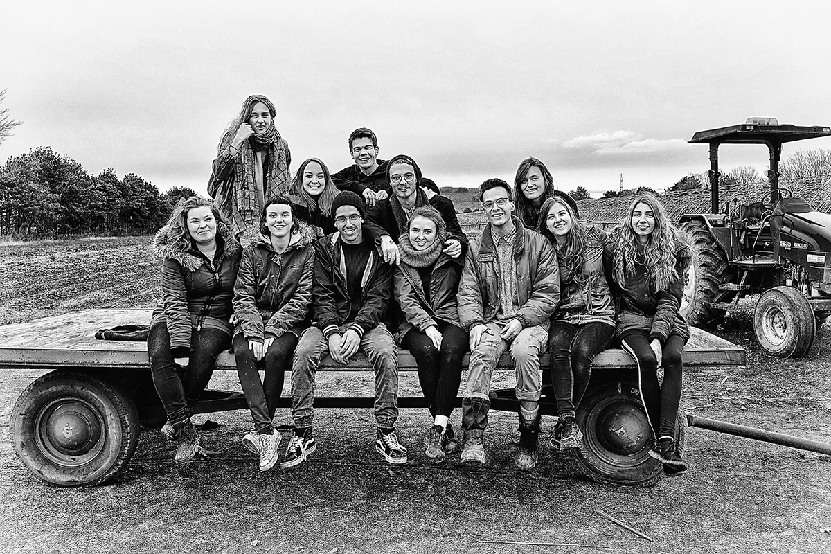 Photo noir et blanc d'un groupe de personnes assises sur une remorque dans un champ.