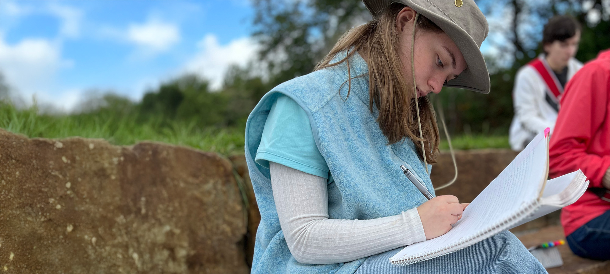 Dans un champ, une jeune femme écrit dans un cahier