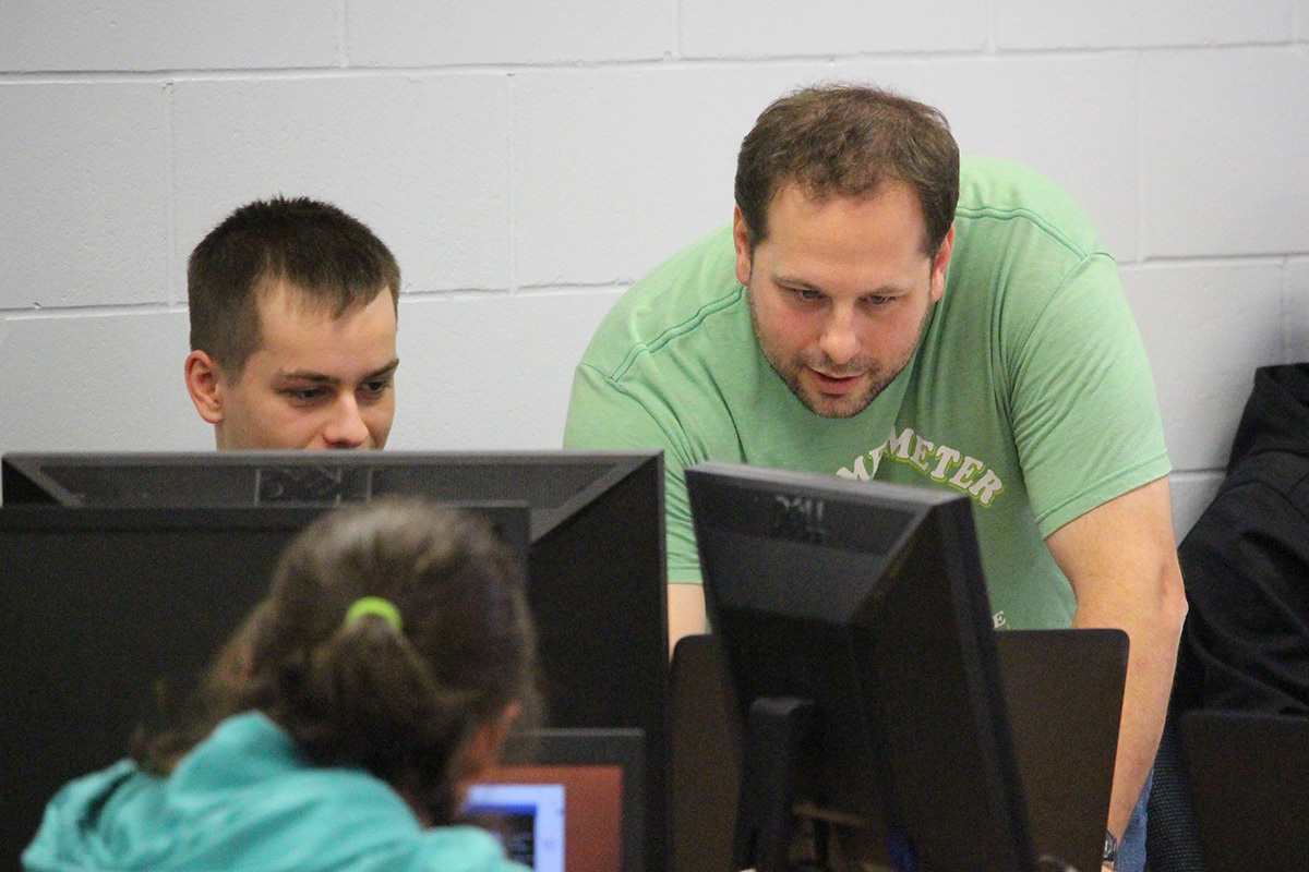 Enseignant en informatique aidant un étudiant face à un écran d'ordinateur
