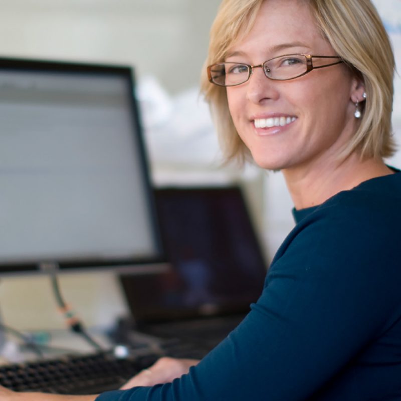 Femme blonde souriante assise devant un écran d'ordinateur