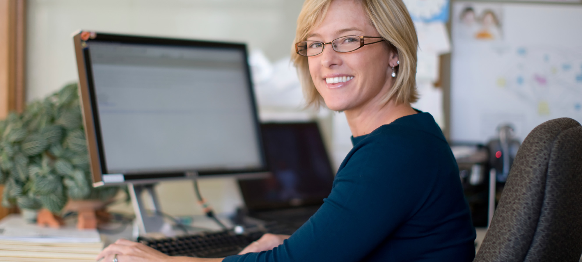 Femme blonde souriante assise devant un écran d'ordinateur