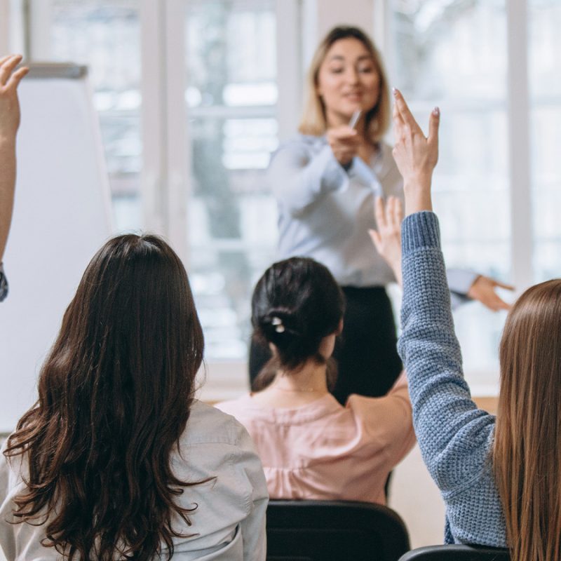 Une enseignante face à une classe d'adultes avec la main levée