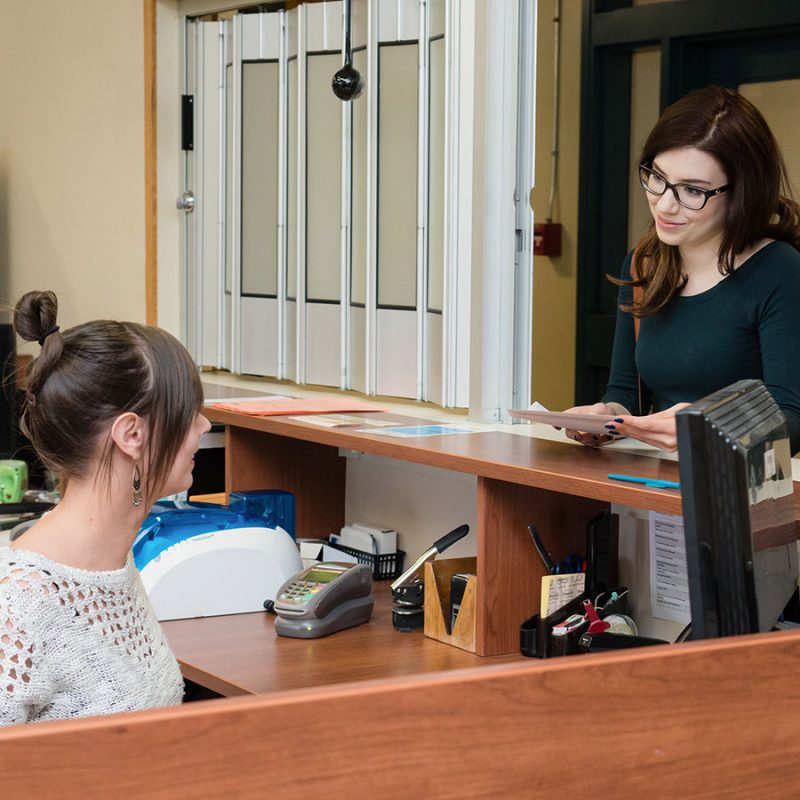 Photo d'une employée au comptoir du registrariat servant une étudiante