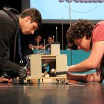 Deux étudiants accroupis apportent les derniers préparatifs à un engin mécanique en compétition