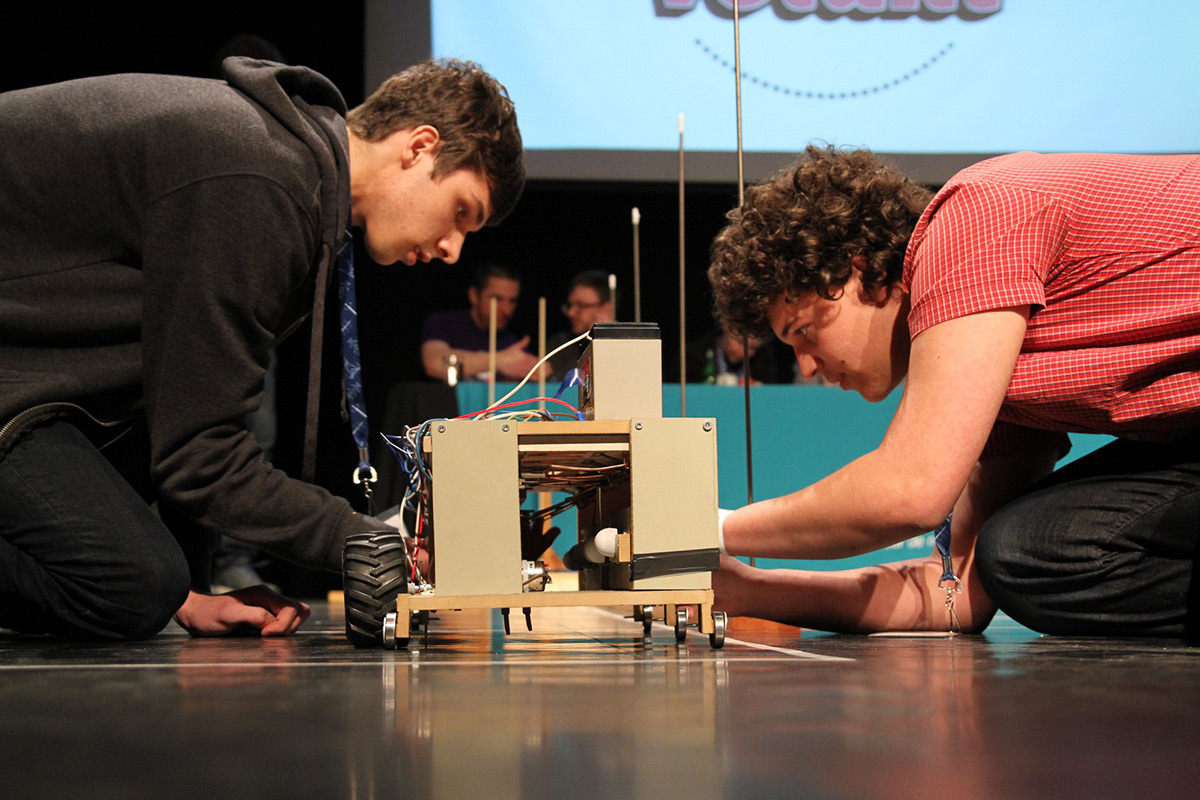 Deux étudiants accroupis apportent les derniers préparatifs à un engin mécanique en compétition