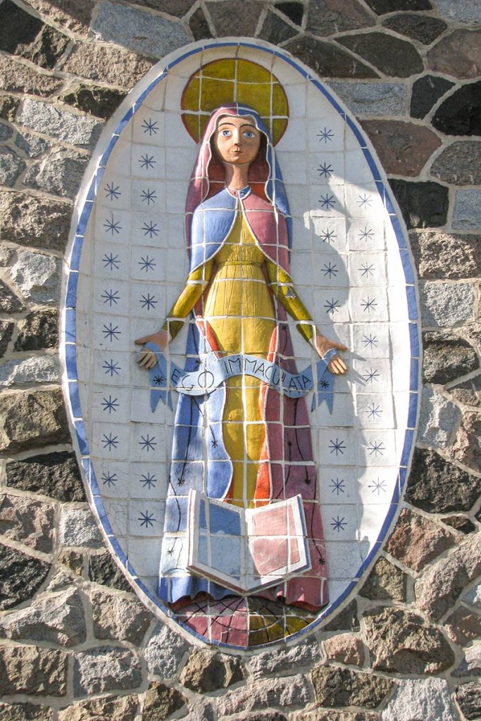 Sur le mur de pierre, la vierge Marie dans un médaillon. L'oeuvre est en mosaïque.