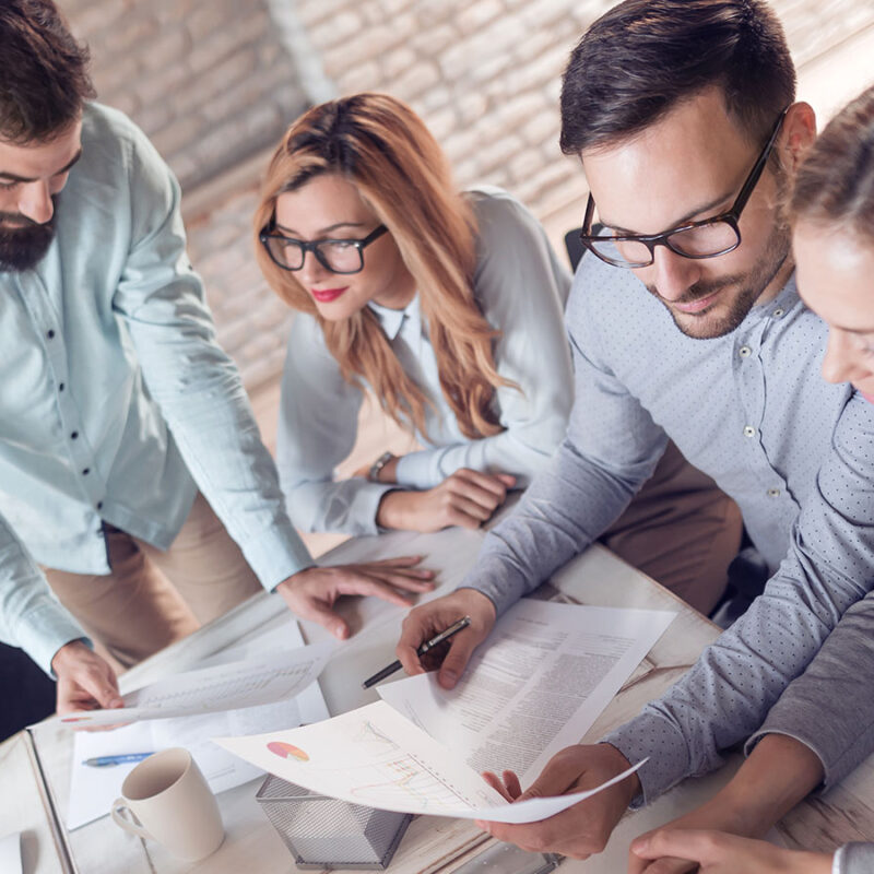 Quatre personnes penchées sur une table de travail où sont des papiers