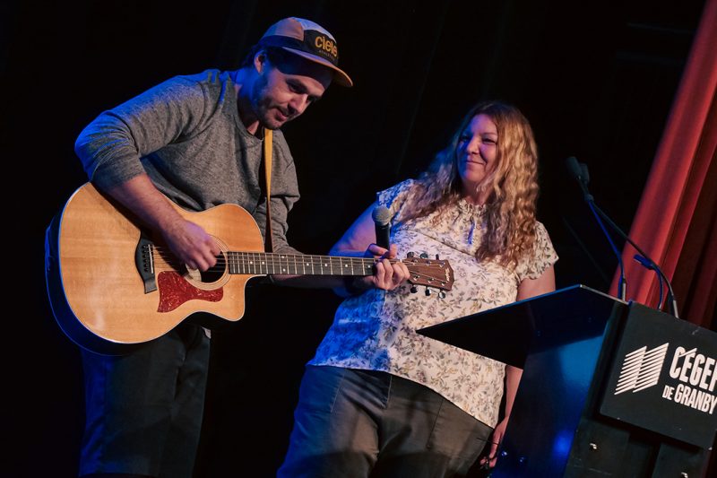 Un musicien avec sa guitare et une femme derrière un lutrin sur une scène