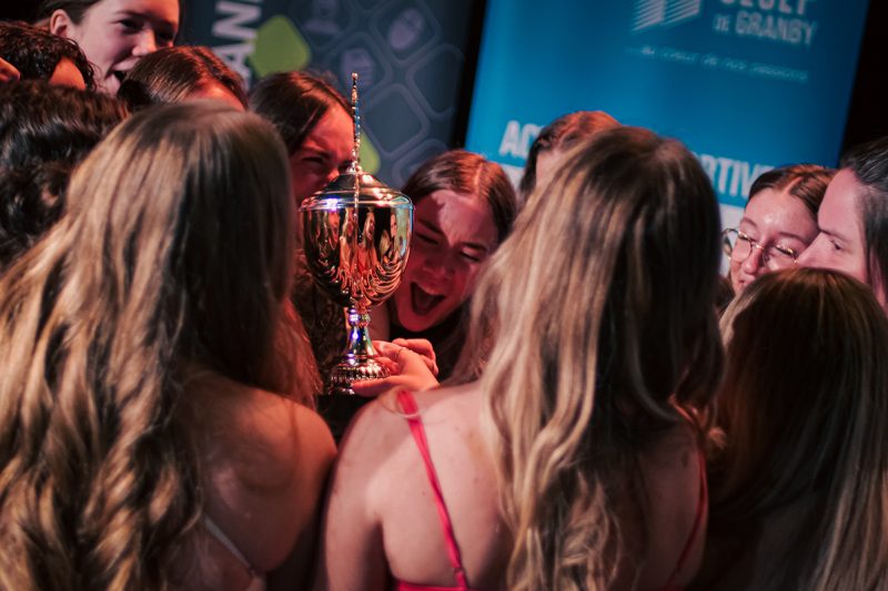 Un groupe des jeunes femmes souriantes autour d'un trophée
