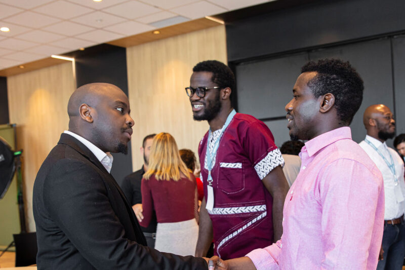 Dans une salle de congrès, trois hommes noirs en conversation