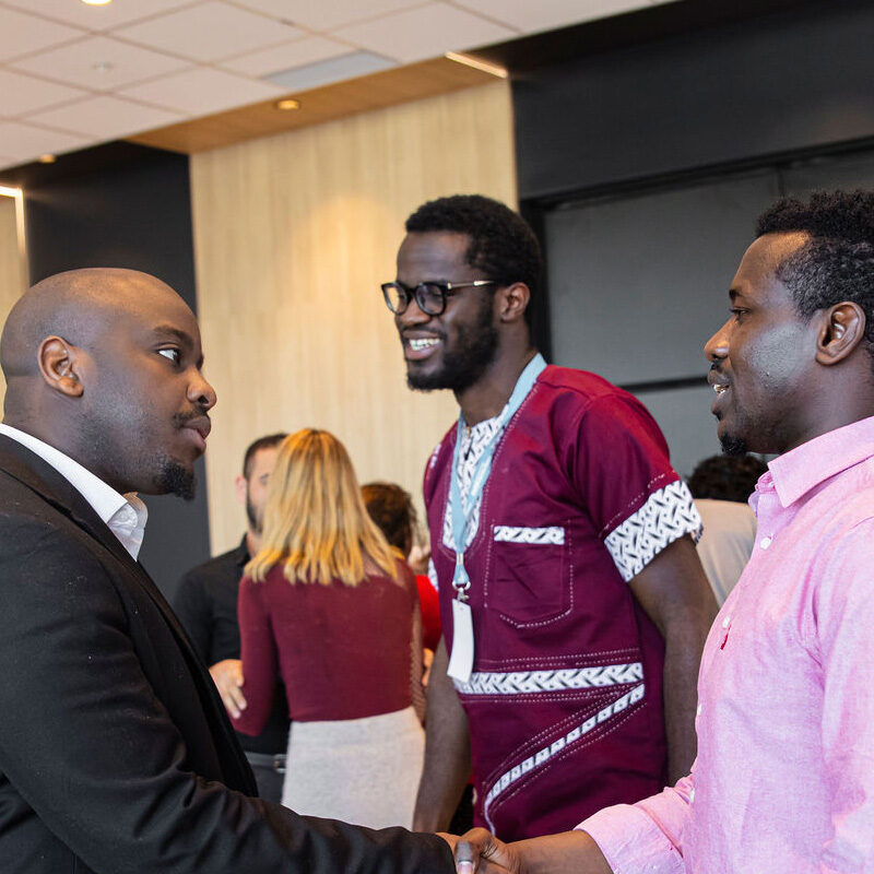 Dans une salle de congrès, trois hommes noirs en conversation