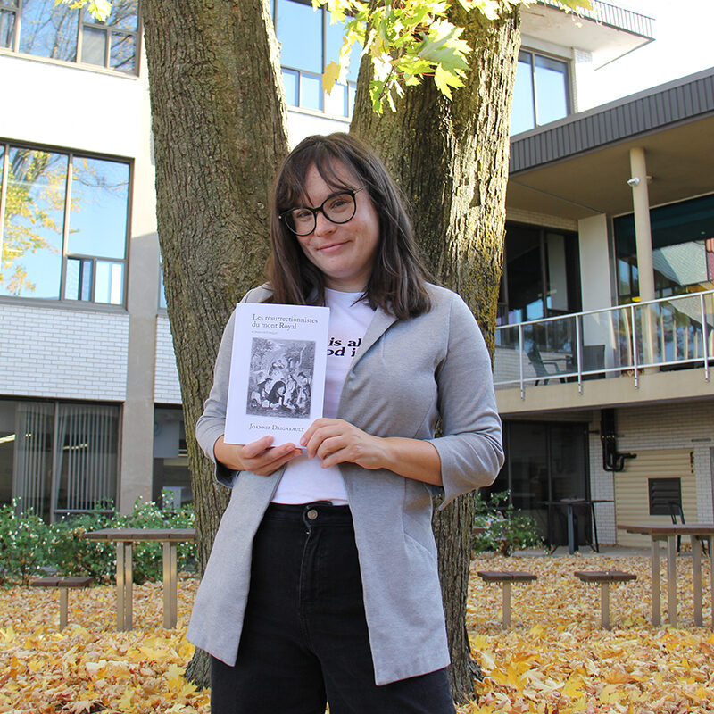 Une jeune autrice tient son livre dans un jardin à l'automne