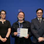 Un homme, encadré par une femme et un homme, tient un certificat en souriant