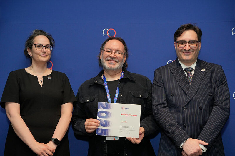 Un homme, encadré par une femme et un homme, tient un certificat en souriant