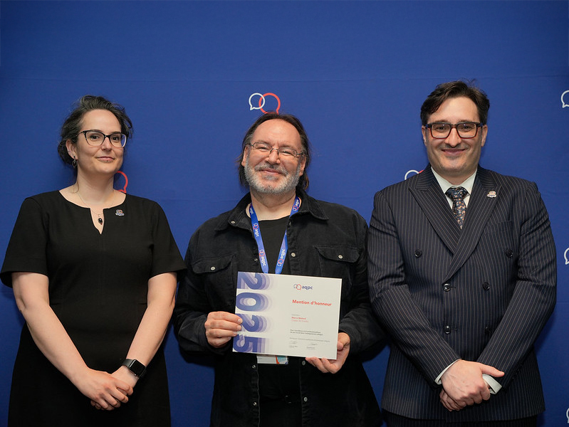 Un homme, encadré par une femme et un homme, tient un certificat en souriant