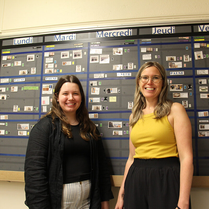 Deux jeunes femmes devant un tableau où est afficher un horaire