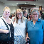 Trois femmes souriantes en avant-plan d'une foule