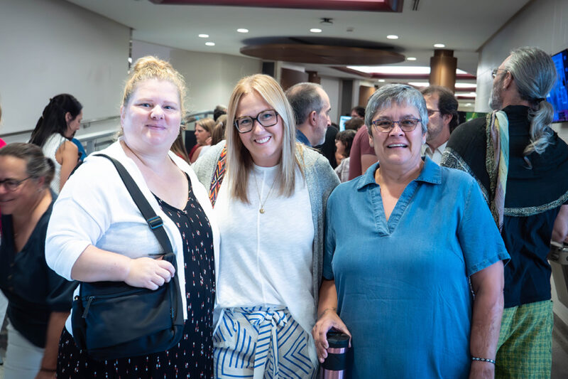 Trois femmes souriantes en avant-plan d'une foule