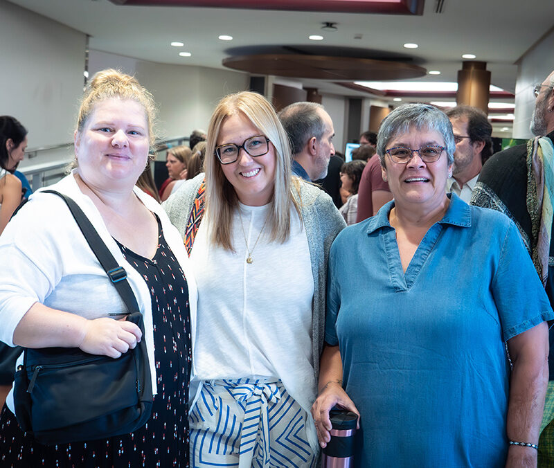 Trois femmes souriantes en avant-plan d'une foule