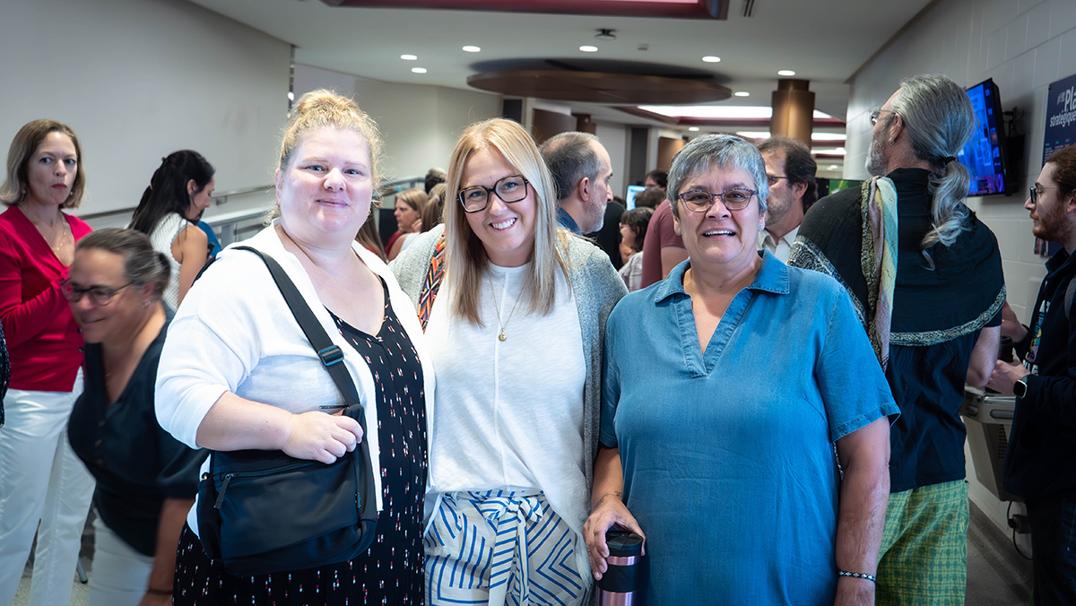 Trois femmes souriantes en avant-plan d'une foule