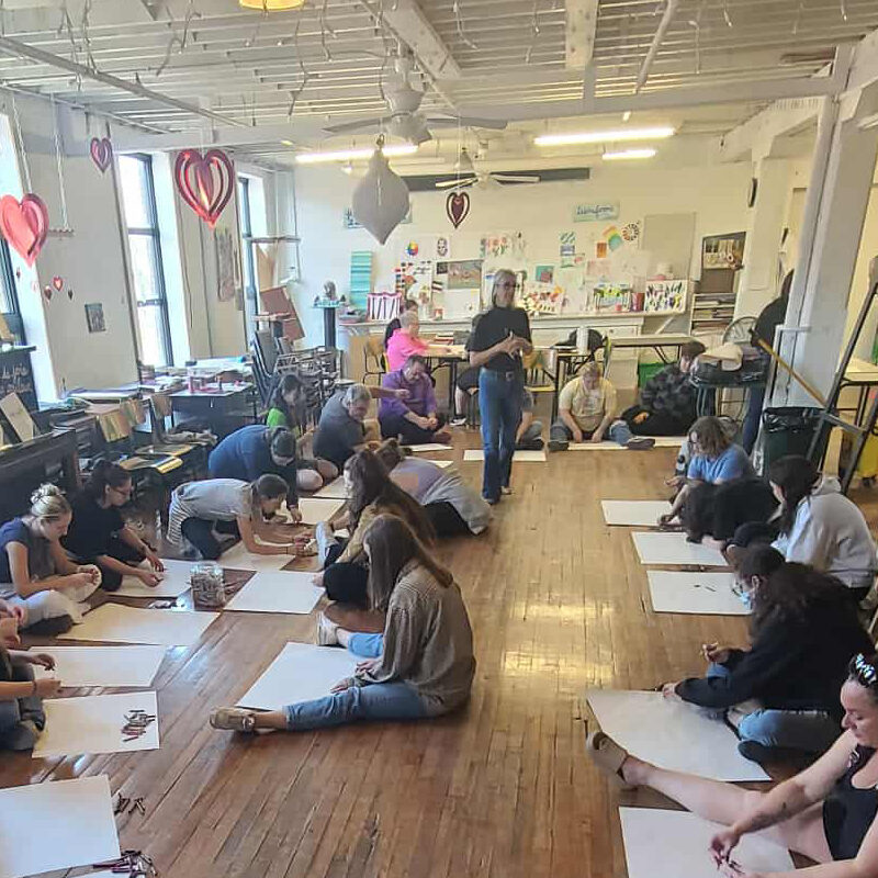 Groupe de personnes assises par terre devant des feuilles pour dessiner.