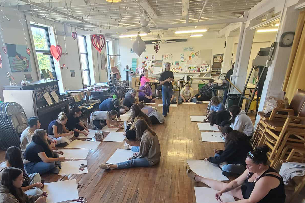 Groupe de personnes assises par terre devant des feuilles pour dessiner.