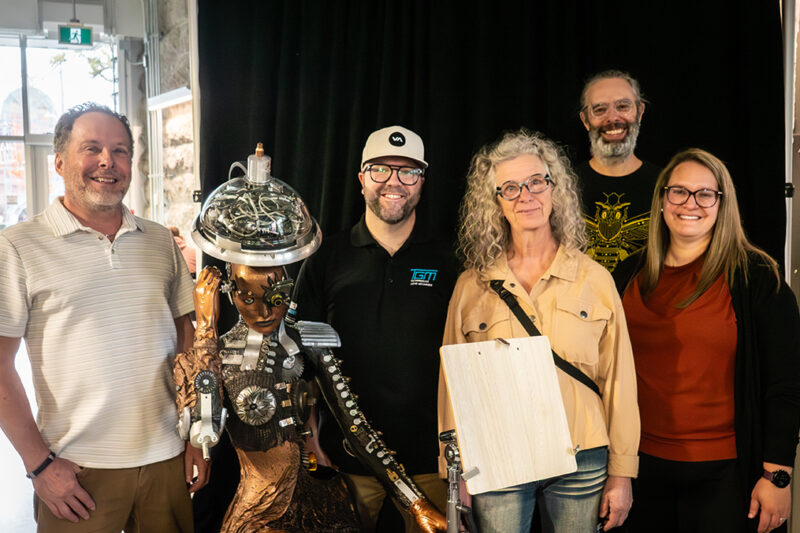 Cinq personnes à côté d'une structure (assemblage) humanoïde