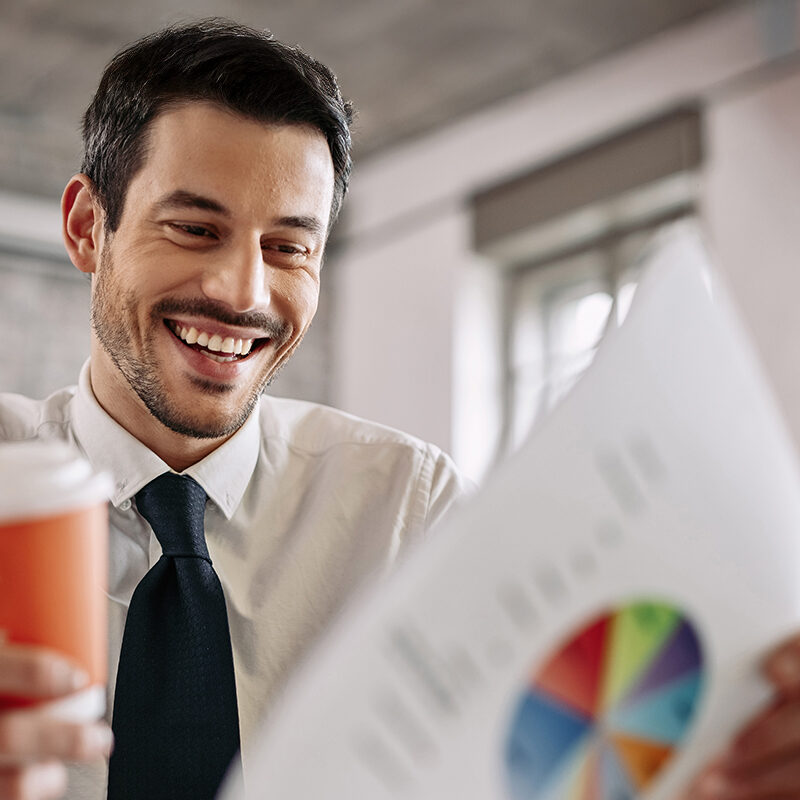 Un homme regarde en souriant un graphique en tenant un café à la main