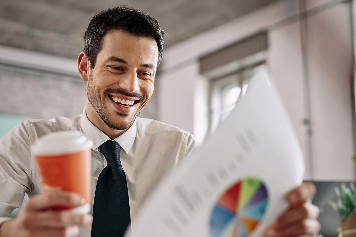 Un homme regarde en souriant un graphique en tenant un café à la main