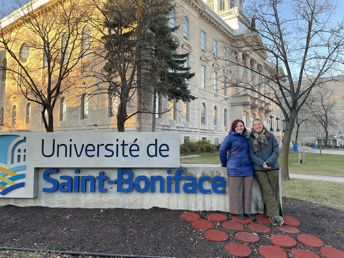 Deux femmes devant l'enseigne de l'Université Saint-Boniface.