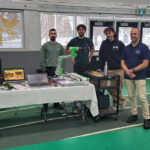Quatre hommes debout à côté d'une table d'exposition technologique