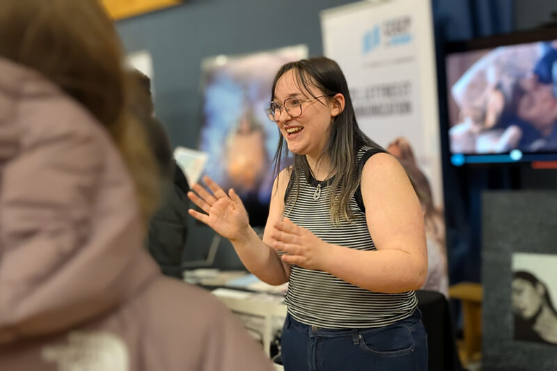 Une jeune femme souriante accueille des visiteurs à un kisoque