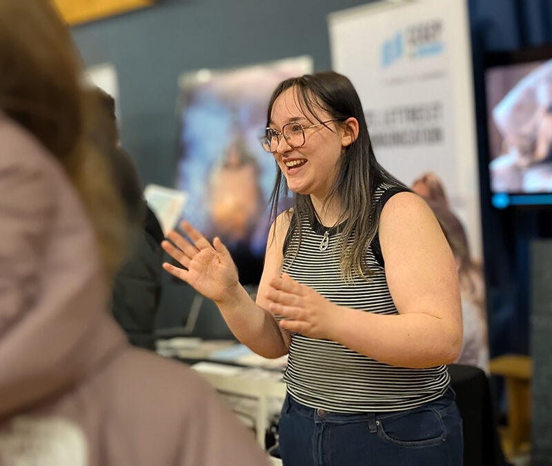 Une jeune femme souriante accueille des visiteurs à un kisoque