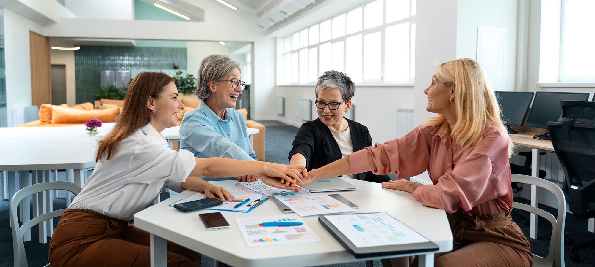 Quatre femmes dans une salle de réunion font un geste de mains empilées