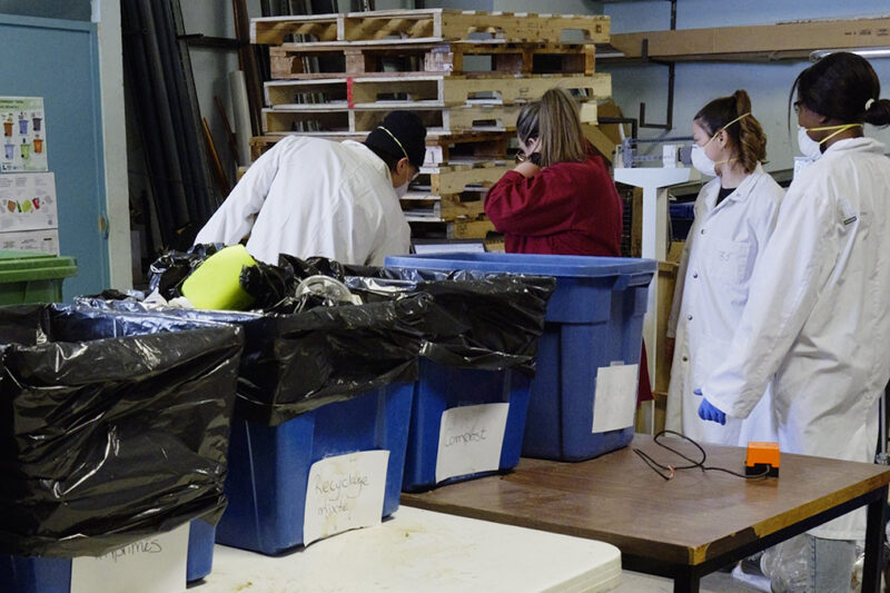 Quatre personnes en sarraus analysent le contenu de bacs de récupération