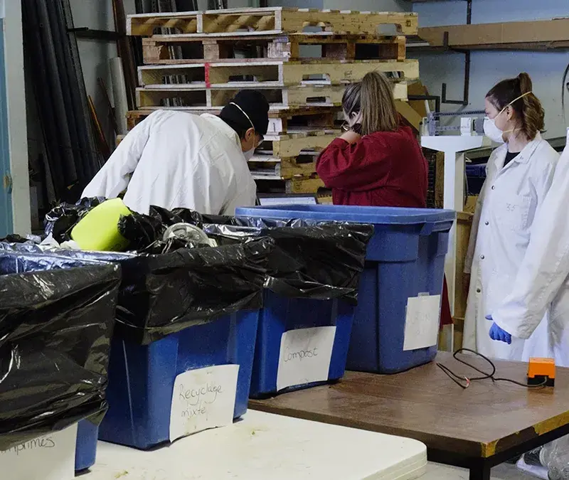 Quatre personnes en sarraus examinent le contenu de bacs de déchets