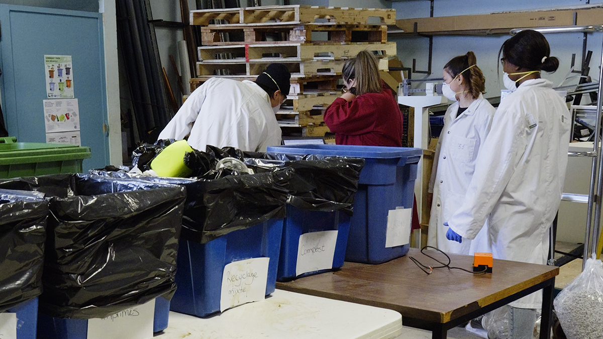Quatre personnes en sarraus analysent le contenu de bacs de récupération