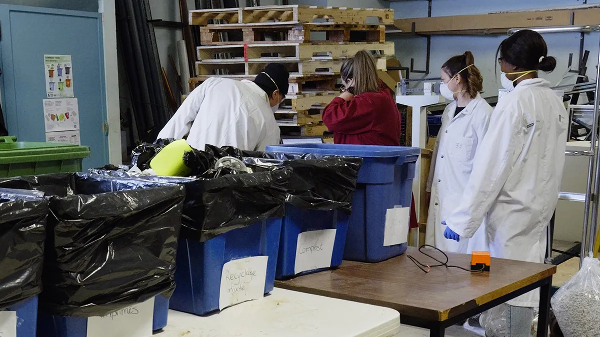 Quatre personnes en sarraus examinent le contenu de bacs de déchets