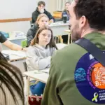 Dans une classe, un homme de dos joue de la guitare à des étudiants