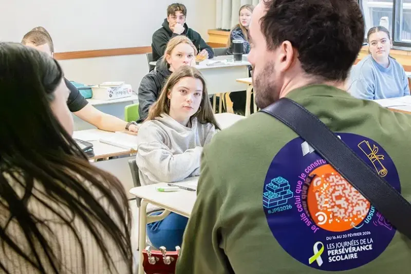Dans une classe, un homme de dos joue de la guitare à des étudiants