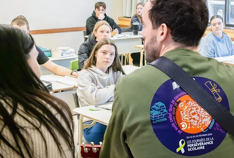 Dans une classe, un homme de dos joue de la guitare à des étudiants