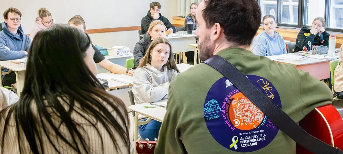 Dans une classe, un homme de dos joue de la guitare à des étudiants