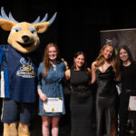 Remise de prix avec une mascotte de cerf et 4 jeunes femmes sur la scène