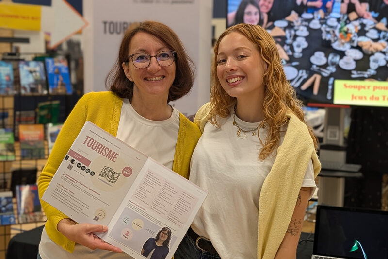 Une femme et une jeune fille à un kiosque d'informaton où est écrit : Tourisme